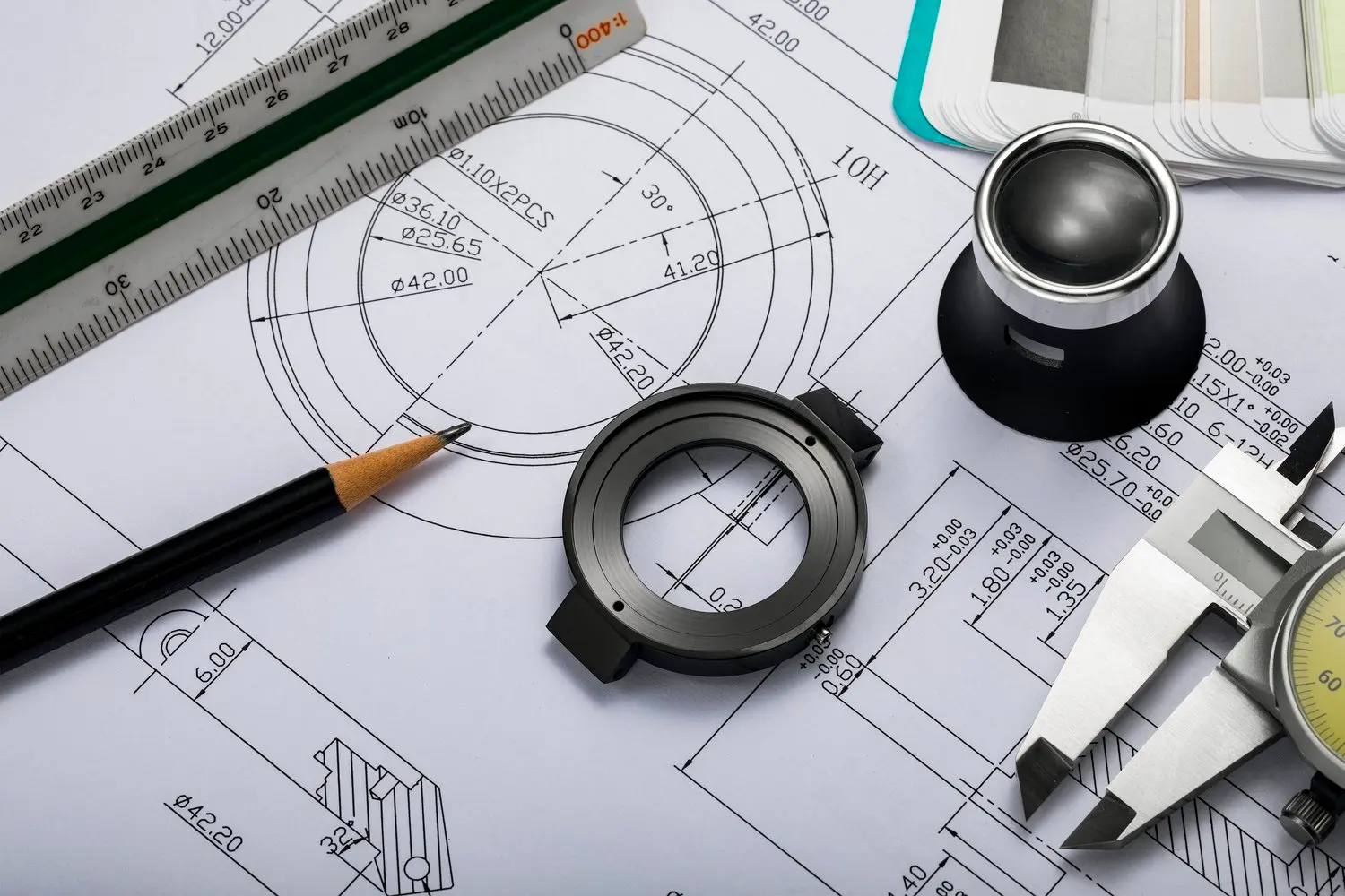Engineering technical drawing with measuring tools, including a ruler, caliper and two rings, on blueprints.