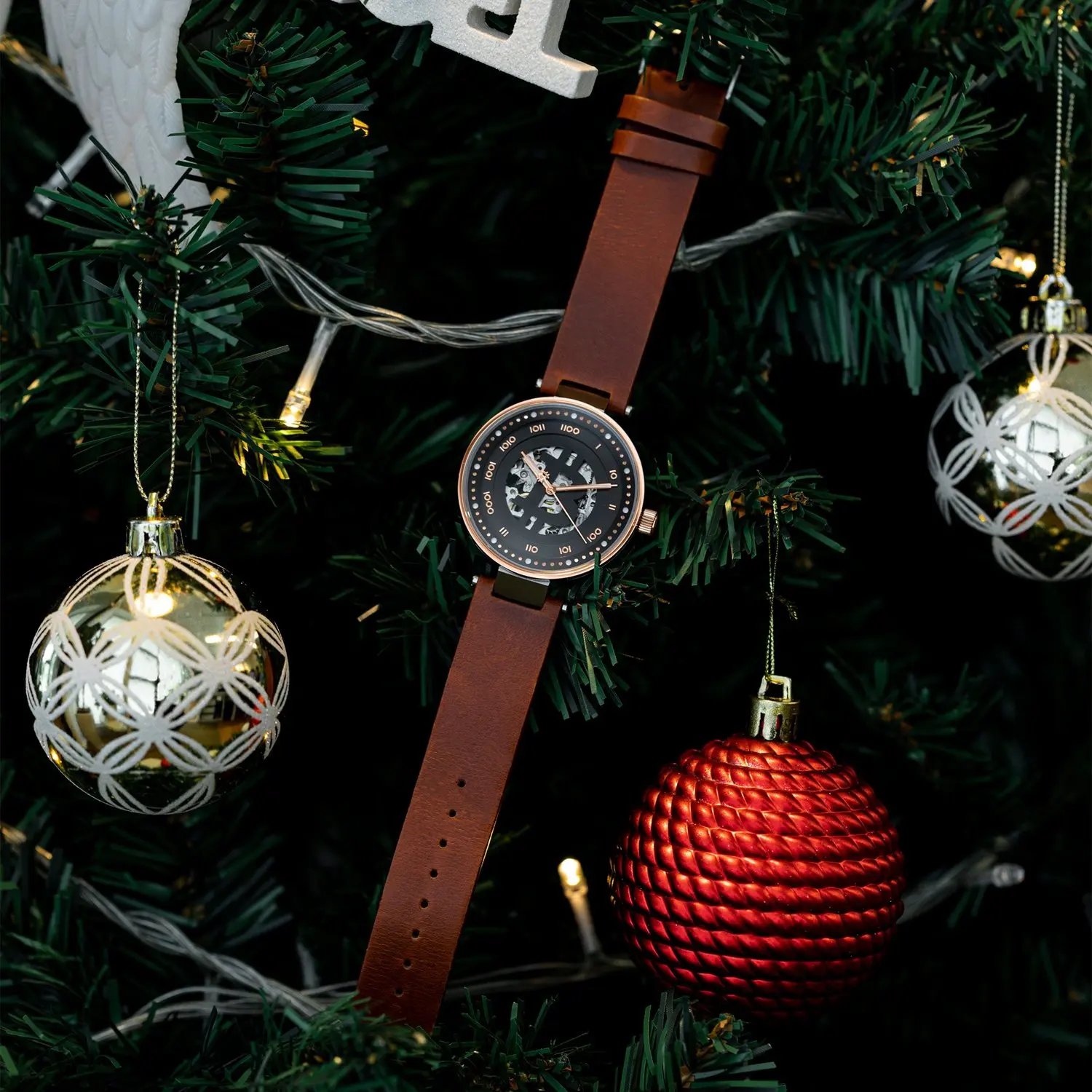 A bitcoin wristwatch with a black face and brown leather strap hanging on a decorated Christmas tree.