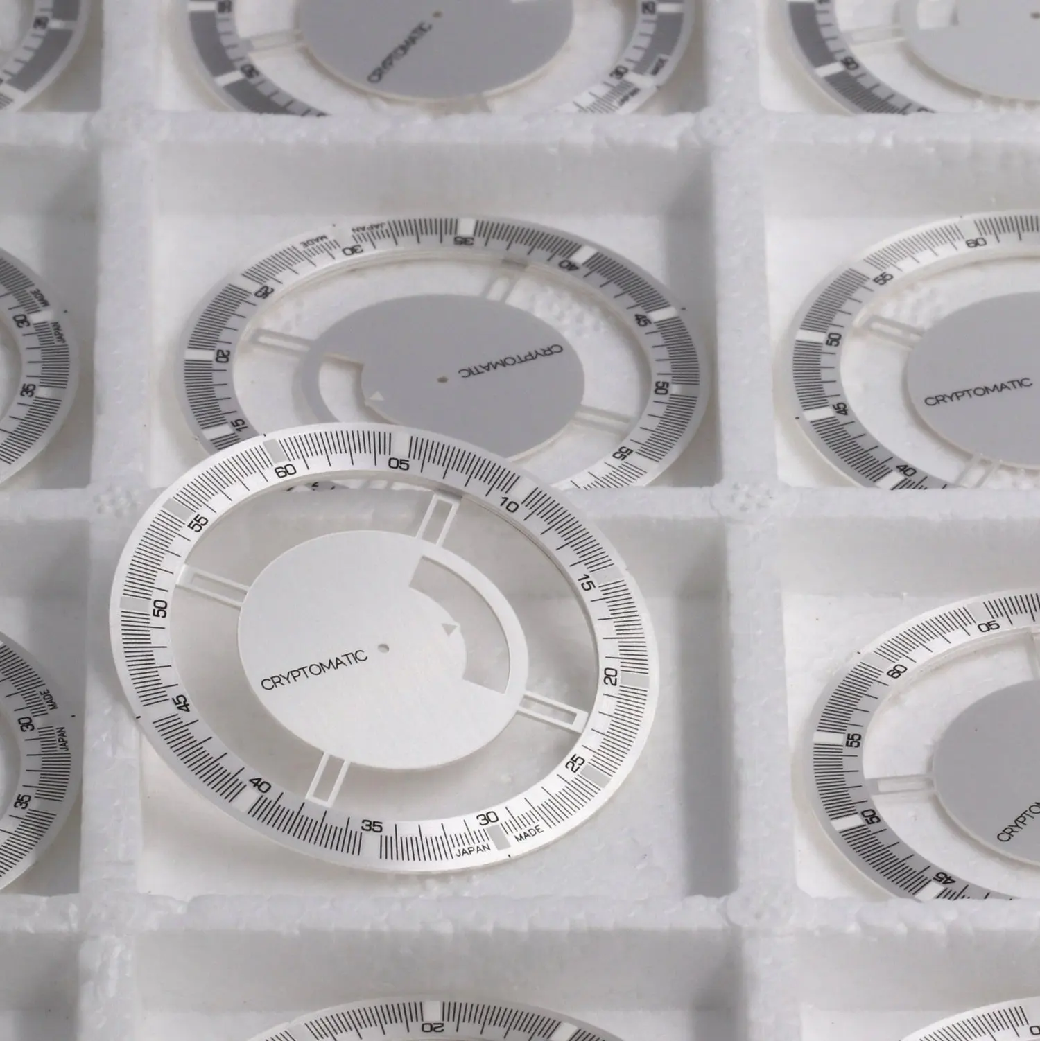 Multiple white bitcoin watch dials with black markings, labeled CRYPTOMATIC, placed in foam packaging.