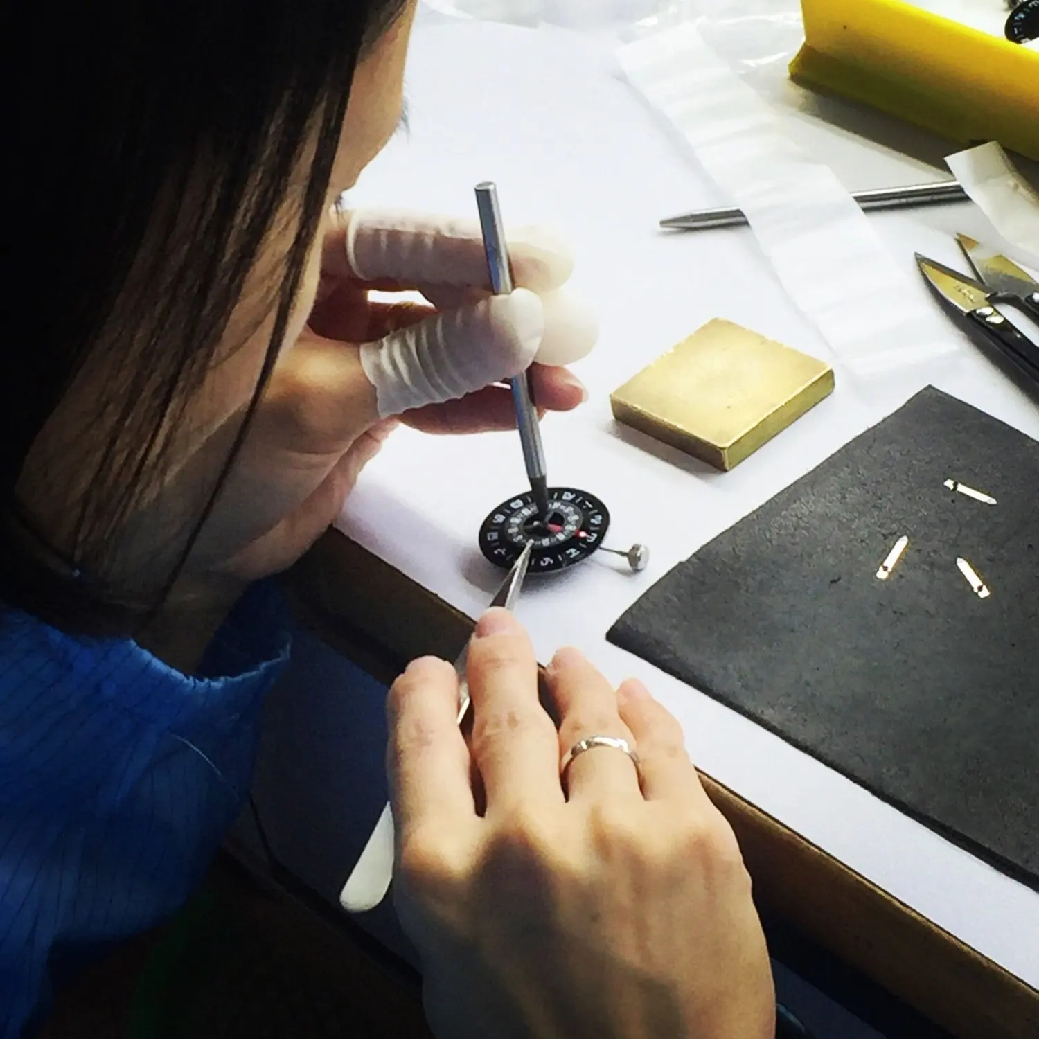 A person working on assembling or repairing a watch, using precision tools on a work surface with various watch parts.