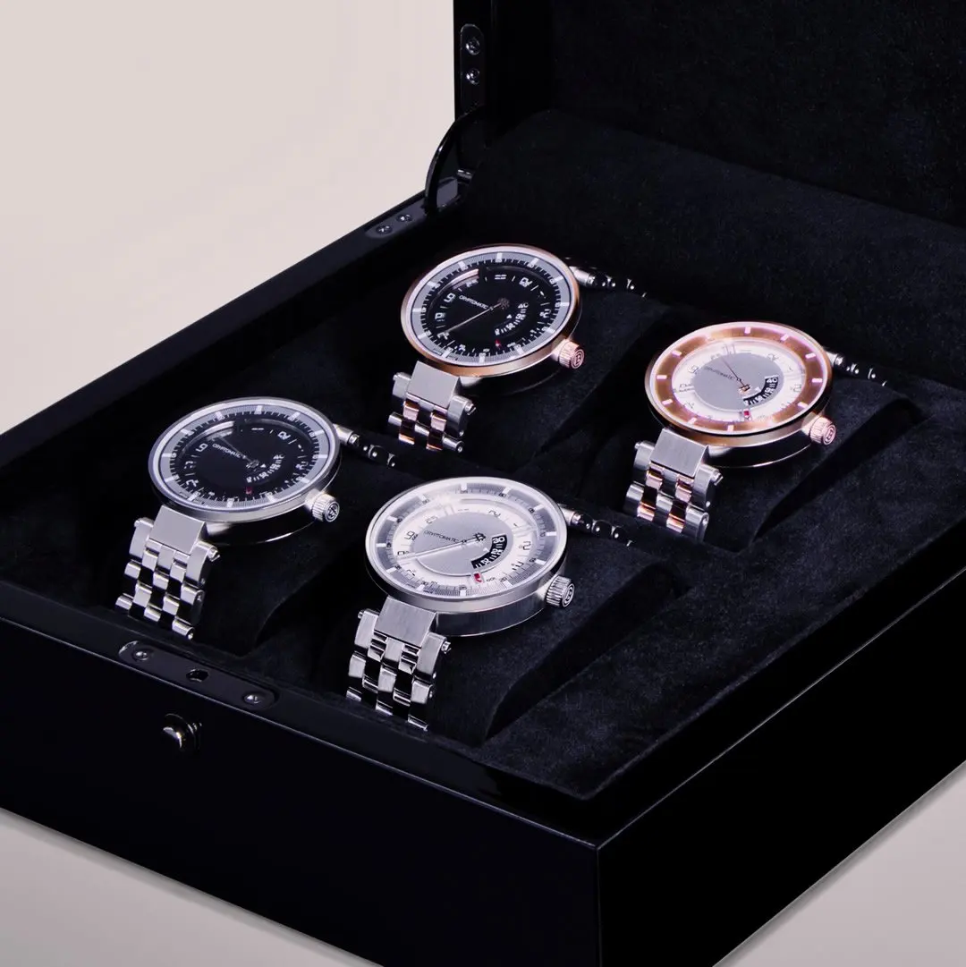 A black box containing five luxury bitcoin wristwatches with metal bands, each placed in individual cushioned compartments.